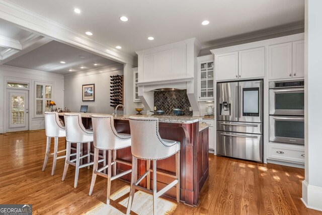 kitchen featuring white cabinetry, hardwood / wood-style flooring, an island with sink, pendant lighting, and crown molding