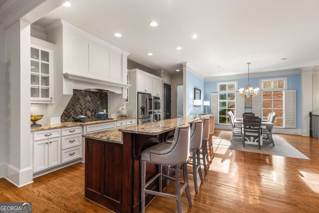 kitchen with hardwood / wood-style floors, pendant lighting, stainless steel appliances, sink, and a kitchen island with sink