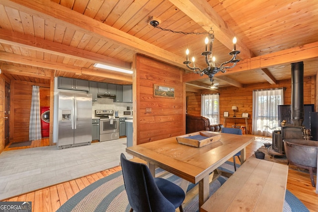 dining space with wood ceiling, light hardwood / wood-style floors, wooden walls, a wood stove, and beam ceiling