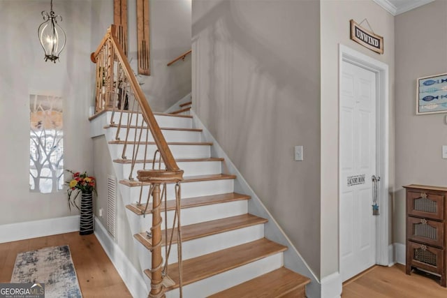 staircase featuring ornamental molding, hardwood / wood-style floors, and a notable chandelier