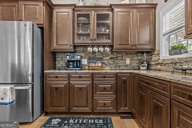 kitchen featuring light wood-type flooring, backsplash, light stone counters, and stainless steel refrigerator