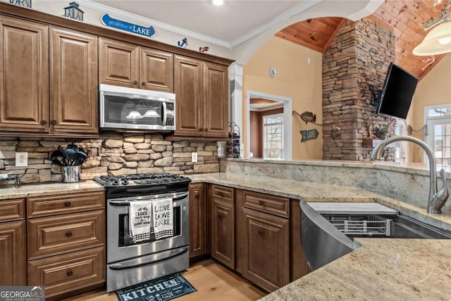 kitchen featuring appliances with stainless steel finishes, tasteful backsplash, light stone countertops, vaulted ceiling, and sink