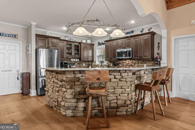 kitchen with kitchen peninsula, appliances with stainless steel finishes, tasteful backsplash, decorative light fixtures, and a kitchen breakfast bar