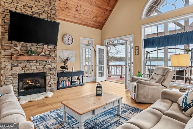 living room featuring high vaulted ceiling, a water view, a stone fireplace, and light hardwood / wood-style floors