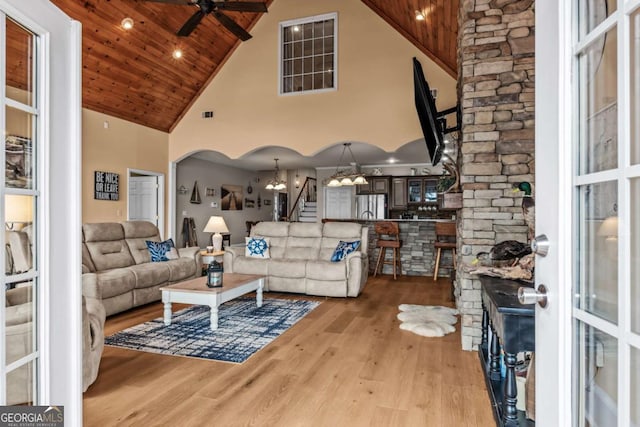 living room featuring high vaulted ceiling, light wood-type flooring, ceiling fan with notable chandelier, and wooden ceiling