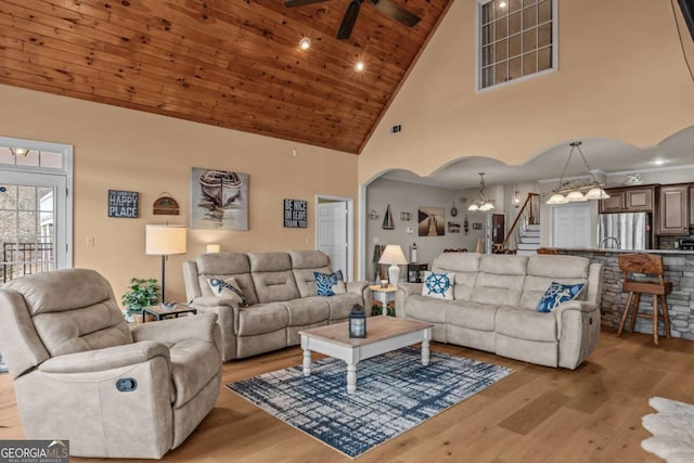 living room with high vaulted ceiling, ceiling fan with notable chandelier, wood ceiling, and light wood-type flooring