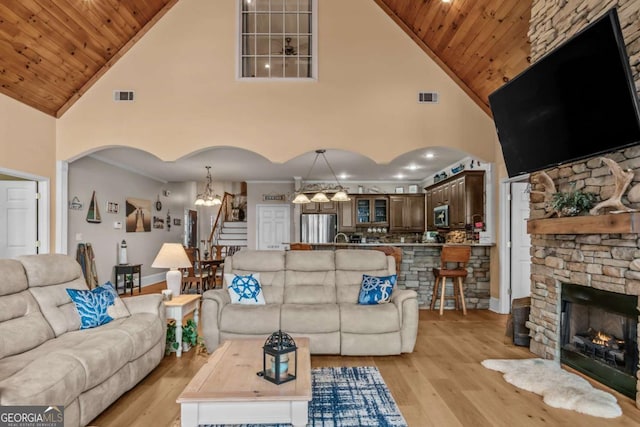 living room with wood ceiling, a stone fireplace, high vaulted ceiling, ornamental molding, and light hardwood / wood-style flooring