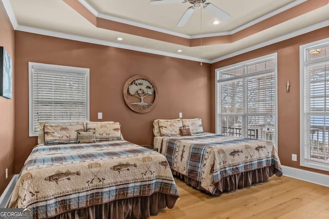 bedroom featuring light wood-type flooring, ceiling fan, crown molding, and a raised ceiling