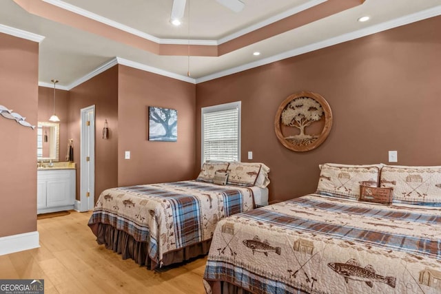 bedroom with connected bathroom, a raised ceiling, ceiling fan, light hardwood / wood-style flooring, and crown molding