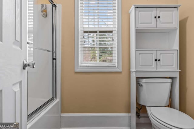 bathroom featuring toilet and bath / shower combo with glass door