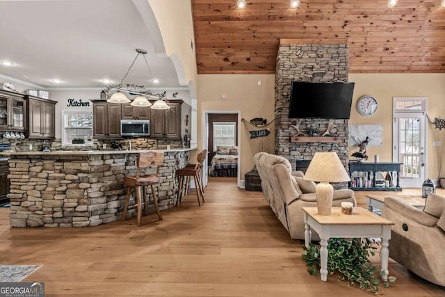 living room with high vaulted ceiling, light hardwood / wood-style flooring, a stone fireplace, and wood ceiling