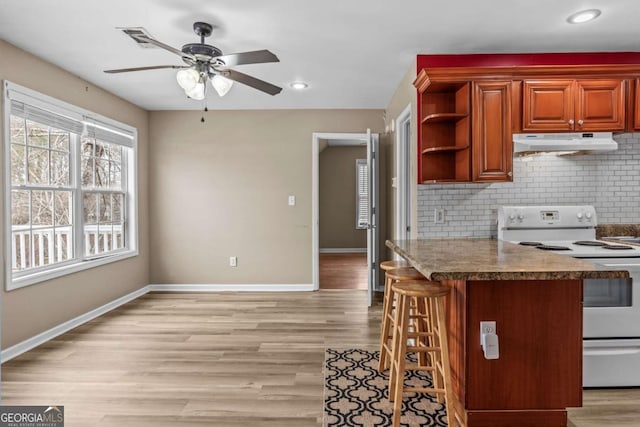 kitchen with electric stove, ceiling fan, tasteful backsplash, light hardwood / wood-style floors, and a breakfast bar