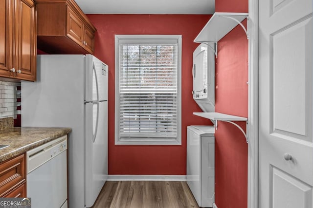 kitchen with light wood-type flooring, stacked washer / dryer, backsplash, and white dishwasher