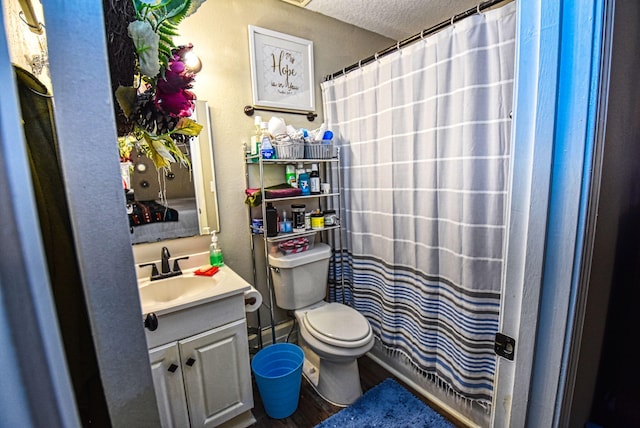 bathroom with a textured ceiling, toilet, walk in shower, and vanity