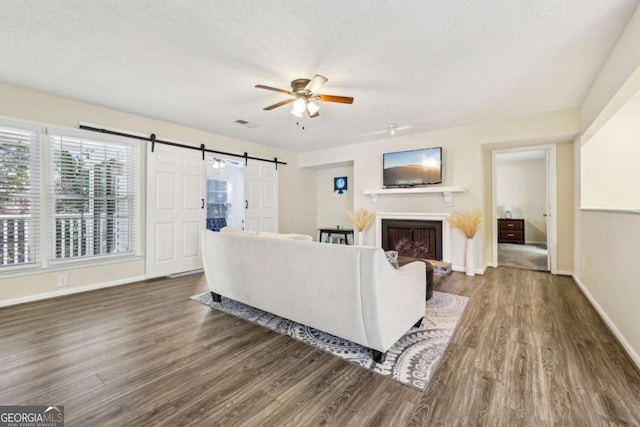 living room with ceiling fan, a barn door, dark wood-type flooring, and a textured ceiling