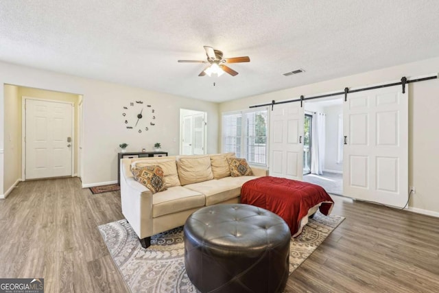 living room with ceiling fan, hardwood / wood-style floors, a textured ceiling, and a barn door