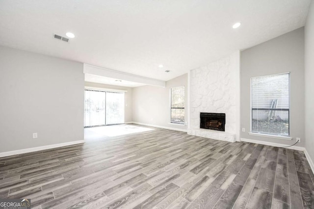 unfurnished living room with lofted ceiling, wood-type flooring, and a stone fireplace