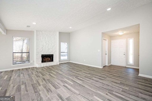 unfurnished living room with lofted ceiling, a fireplace, a textured ceiling, and hardwood / wood-style floors