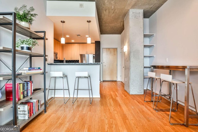 kitchen with a breakfast bar area, appliances with stainless steel finishes, light brown cabinets, light wood-type flooring, and hanging light fixtures