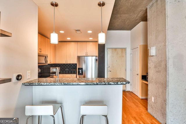 kitchen featuring decorative light fixtures, kitchen peninsula, stainless steel appliances, and light brown cabinetry