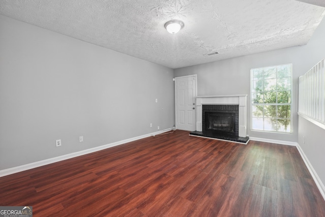 unfurnished living room with a textured ceiling, dark wood-type flooring, and a brick fireplace