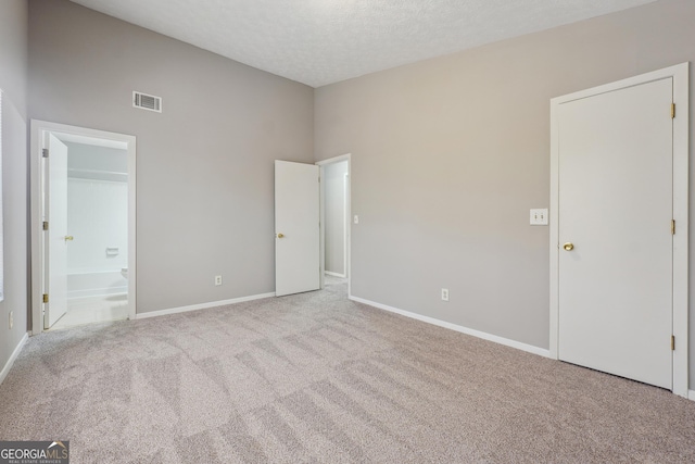 unfurnished bedroom featuring ensuite bath, light carpet, and a textured ceiling