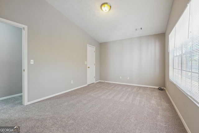 carpeted empty room featuring vaulted ceiling and a textured ceiling