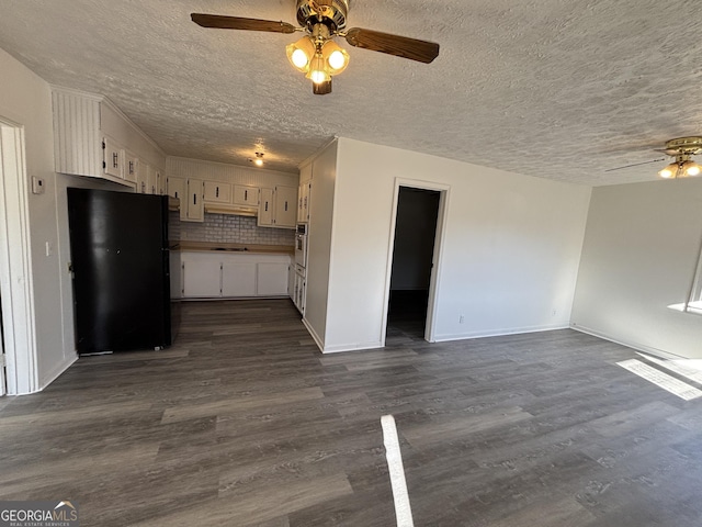 kitchen with white cabinetry, black refrigerator, decorative backsplash, stainless steel oven, and dark hardwood / wood-style flooring