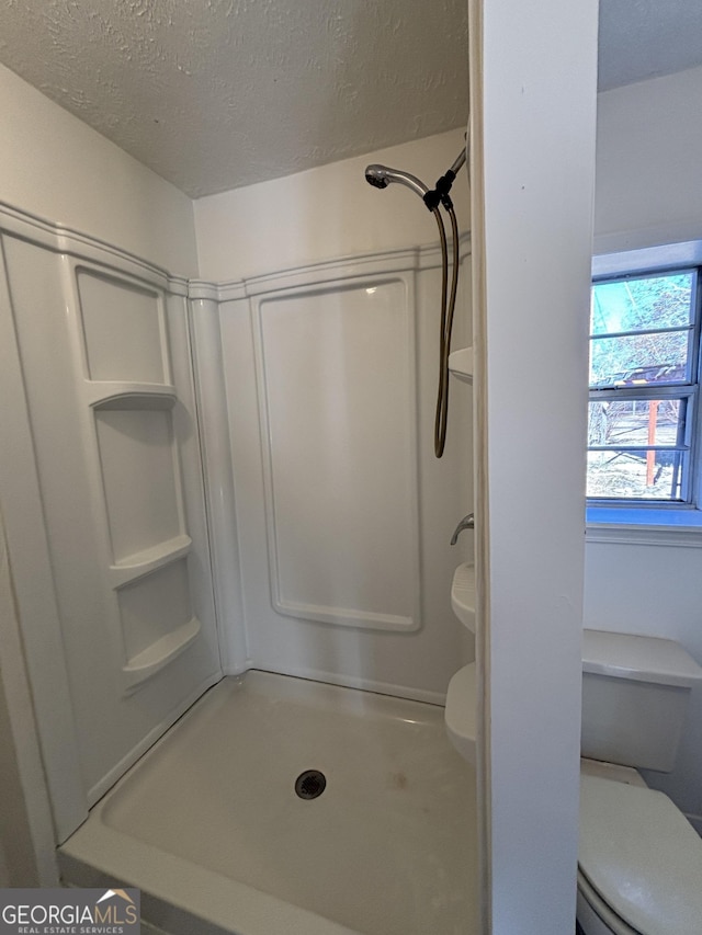 bathroom with a textured ceiling, toilet, and walk in shower