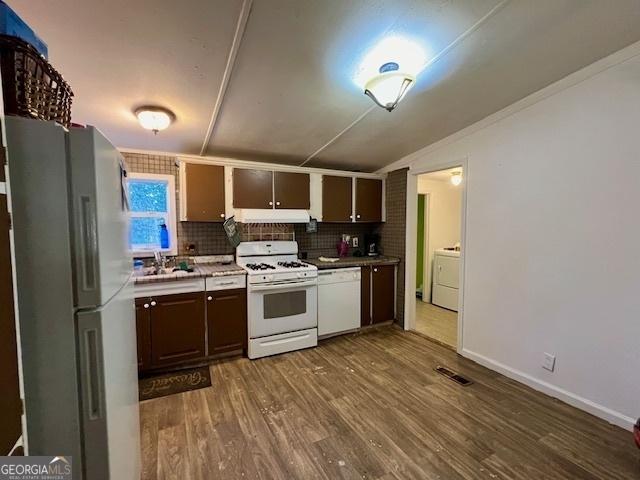 kitchen with washer / dryer, dark brown cabinets, white appliances, hardwood / wood-style floors, and decorative backsplash