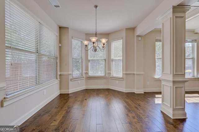 unfurnished dining area with dark wood-type flooring, ornate columns, a chandelier, and a healthy amount of sunlight