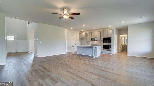 kitchen featuring light wood-type flooring, a kitchen island with sink, stainless steel appliances, and ceiling fan