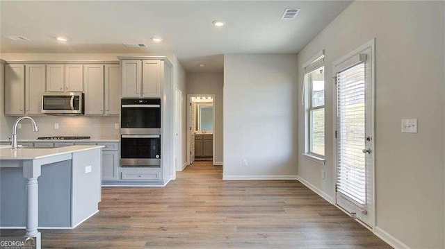 kitchen with appliances with stainless steel finishes, gray cabinetry, light hardwood / wood-style flooring, and plenty of natural light