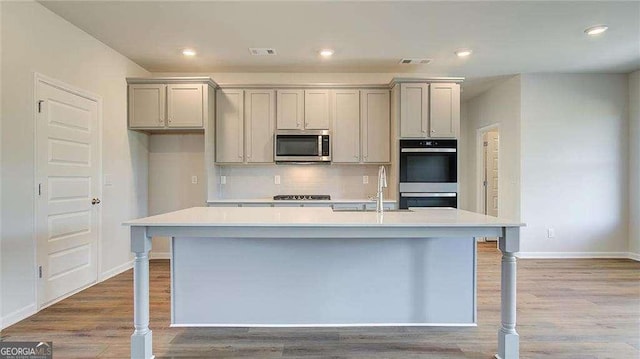 kitchen featuring light wood-type flooring, gray cabinetry, stainless steel appliances, and an island with sink