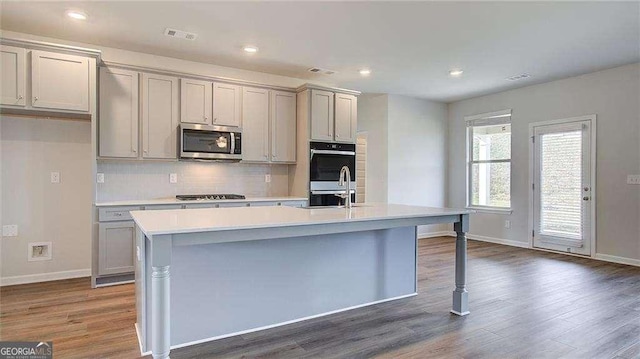 kitchen featuring dark wood-type flooring, gray cabinetry, stainless steel appliances, and an island with sink