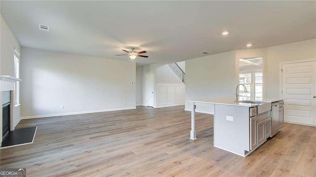 kitchen featuring dishwasher, a kitchen island with sink, light wood-type flooring, ceiling fan, and a breakfast bar area