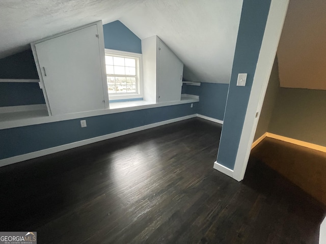 additional living space featuring a textured ceiling, dark wood-type flooring, and lofted ceiling