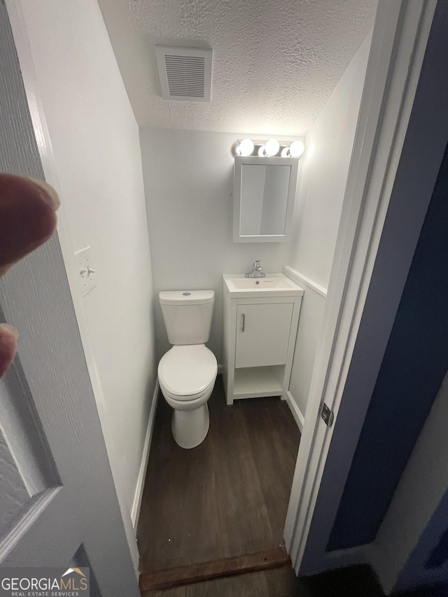 bathroom with wood-type flooring, a textured ceiling, toilet, and vanity