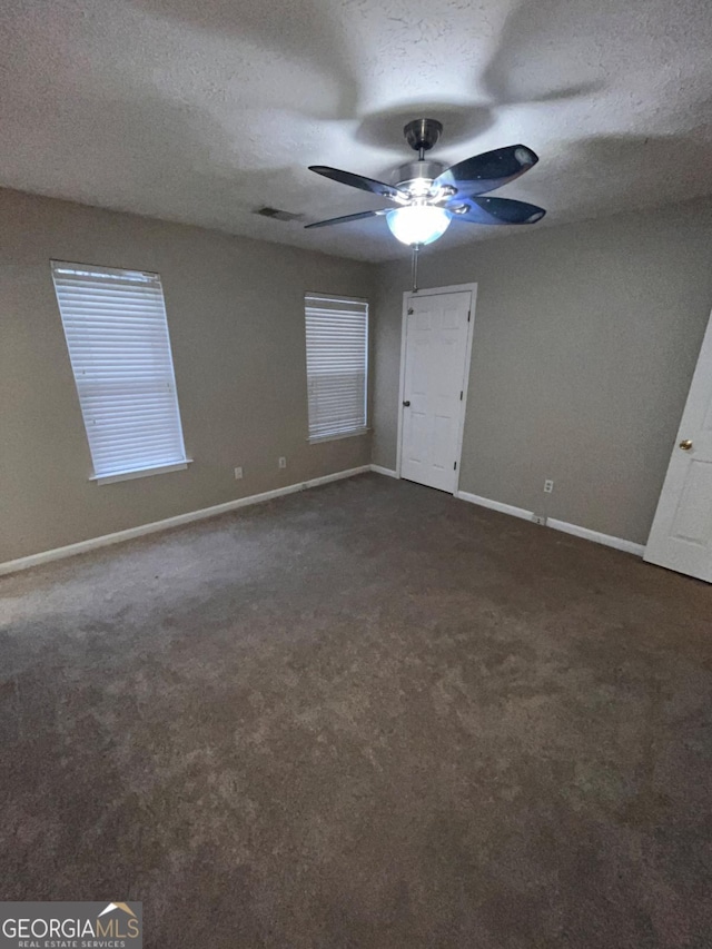 unfurnished room featuring ceiling fan, dark carpet, and a textured ceiling