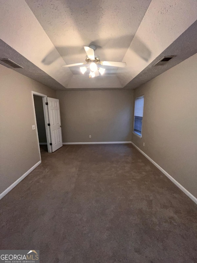 empty room featuring a raised ceiling, a textured ceiling, and dark colored carpet