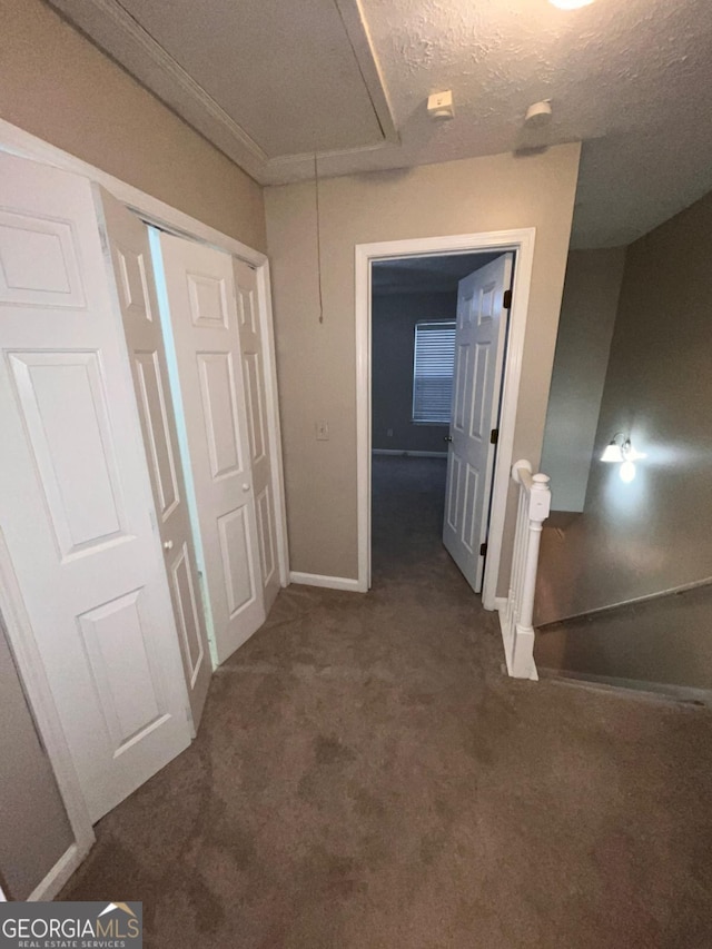 corridor with a textured ceiling and dark colored carpet