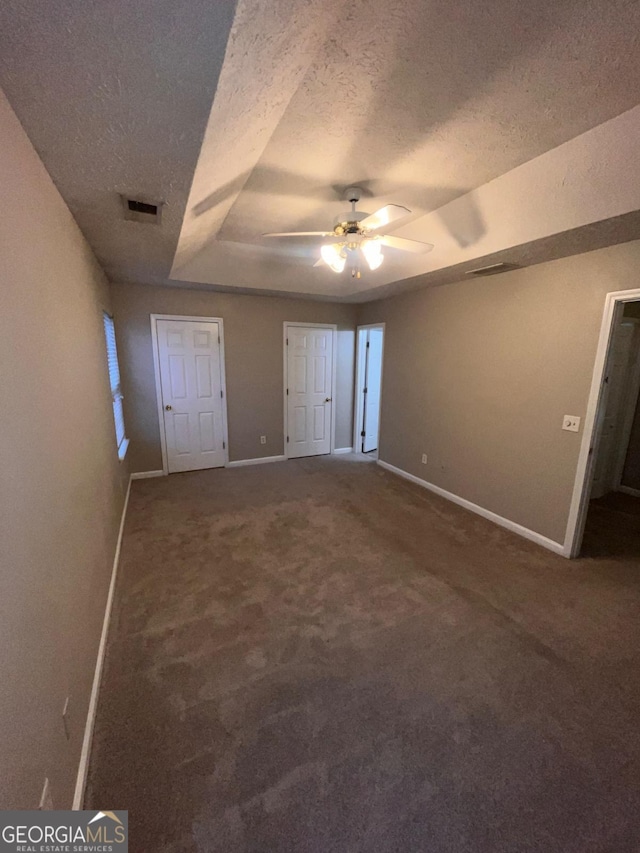 unfurnished bedroom featuring ceiling fan, a raised ceiling, carpet floors, and a textured ceiling