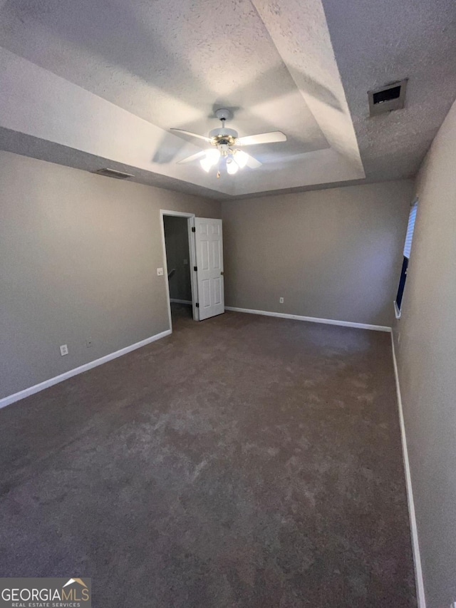 unfurnished bedroom with ceiling fan, a raised ceiling, a textured ceiling, and dark colored carpet