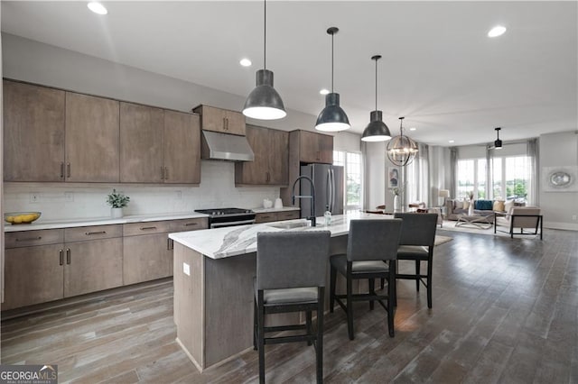 kitchen with an island with sink, appliances with stainless steel finishes, decorative backsplash, hanging light fixtures, and a breakfast bar