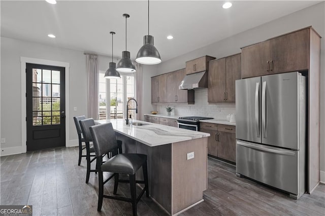 kitchen featuring an island with sink, appliances with stainless steel finishes, pendant lighting, a breakfast bar, and sink