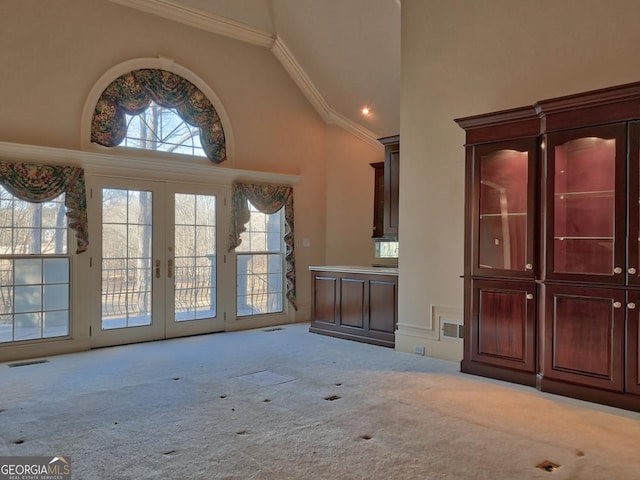 unfurnished living room with high vaulted ceiling, light carpet, ornamental molding, and french doors