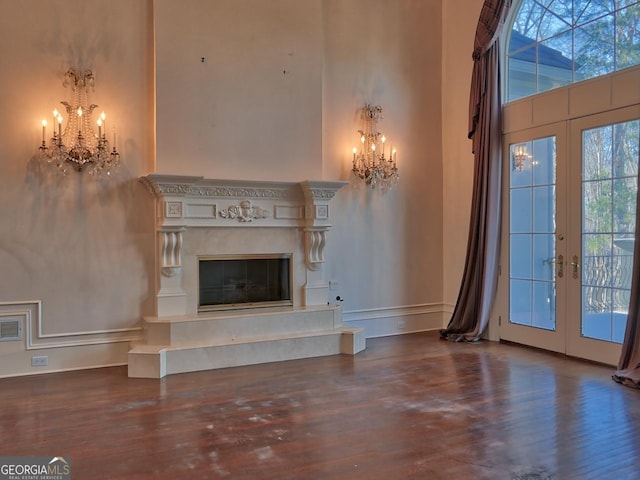 unfurnished living room with wood-type flooring, a high end fireplace, french doors, and an inviting chandelier