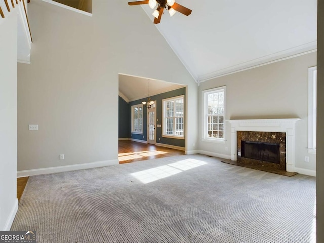 unfurnished living room with high vaulted ceiling, a high end fireplace, ceiling fan with notable chandelier, and carpet floors