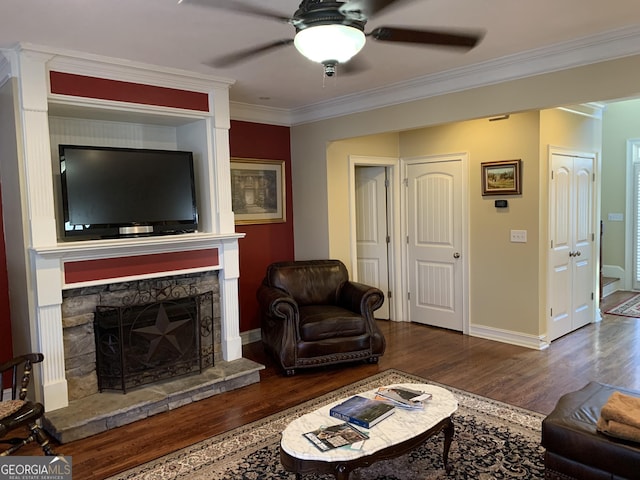 living room featuring ceiling fan, dark wood-type flooring, crown molding, and a stone fireplace