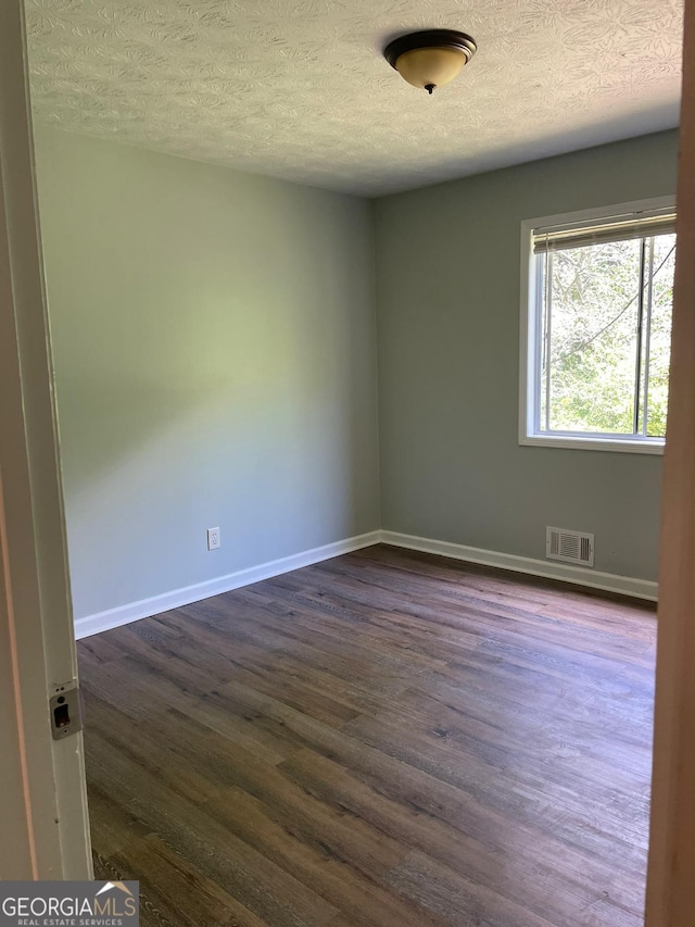 empty room with a textured ceiling and dark hardwood / wood-style floors